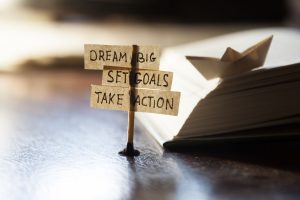 Matchstick holding up paper that says Dream Big, Set Goals, and Take Action