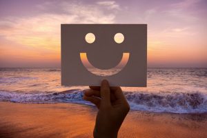 Person's hand holding up a smiley cardboard at the beach, happy to break up life routine