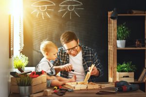 Man at a desk showing his young toddler how to do carpentry