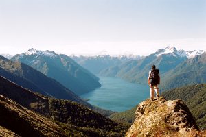 Person standing on mountaintop looking at breathtaking view of water trying to find inspiration