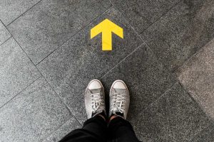 Person's feet standing before an arrow pointing forward showing how to get there